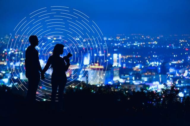 2 silhouettes on a hill overlooking a city 