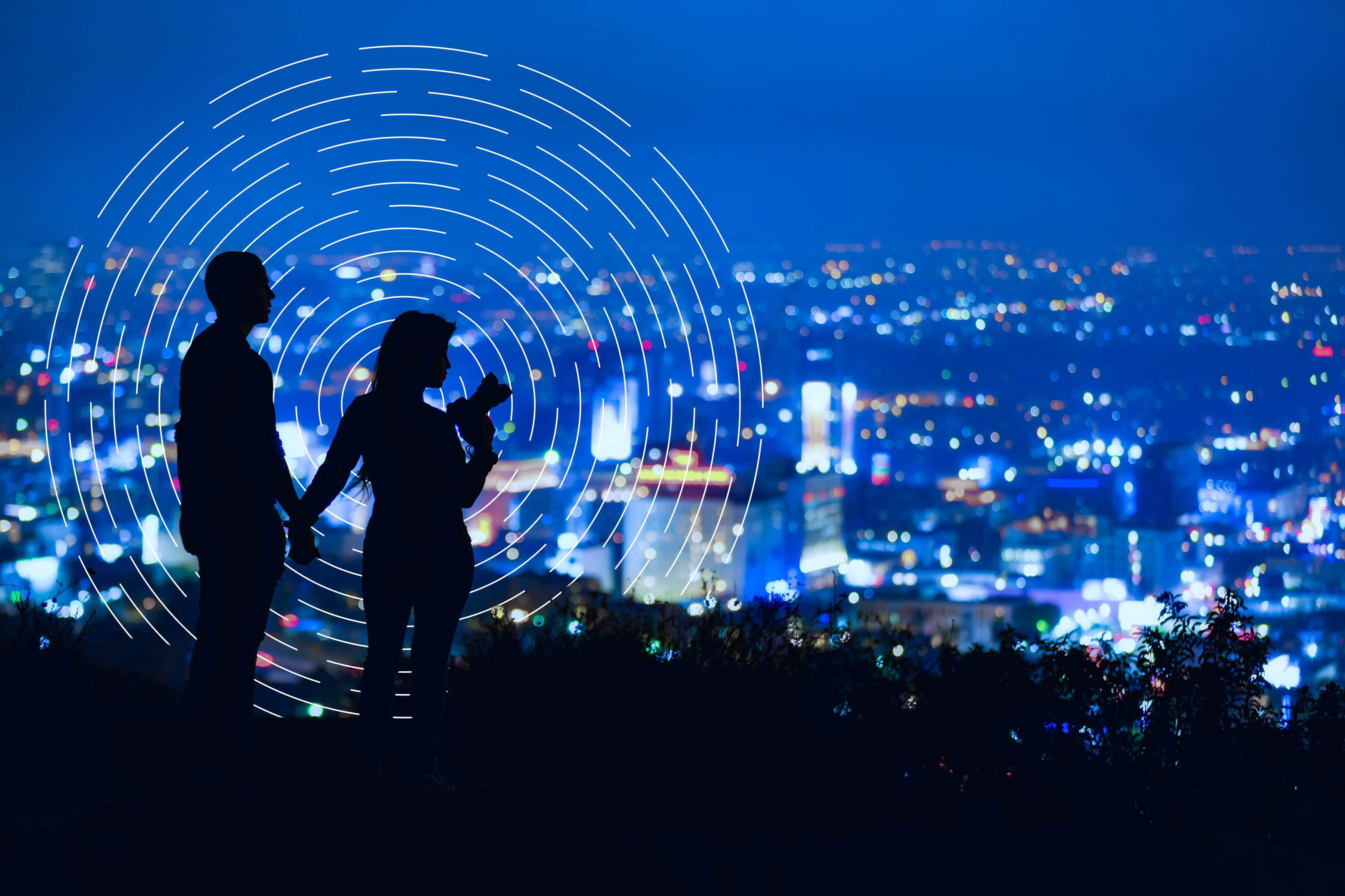 2 silhouettes on a hill overlooking a city 