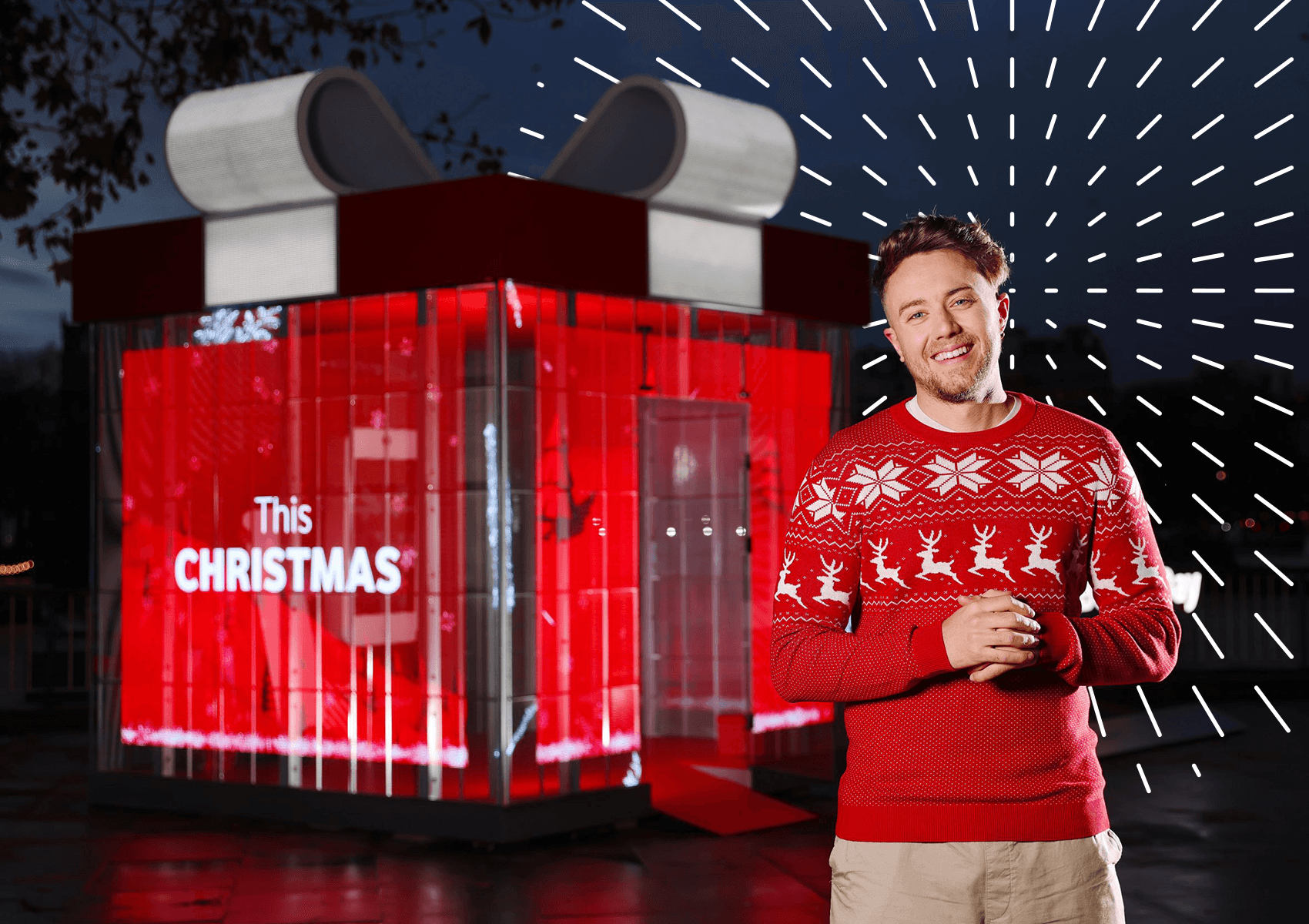 Man in Christmas jumper standing in front of giant present